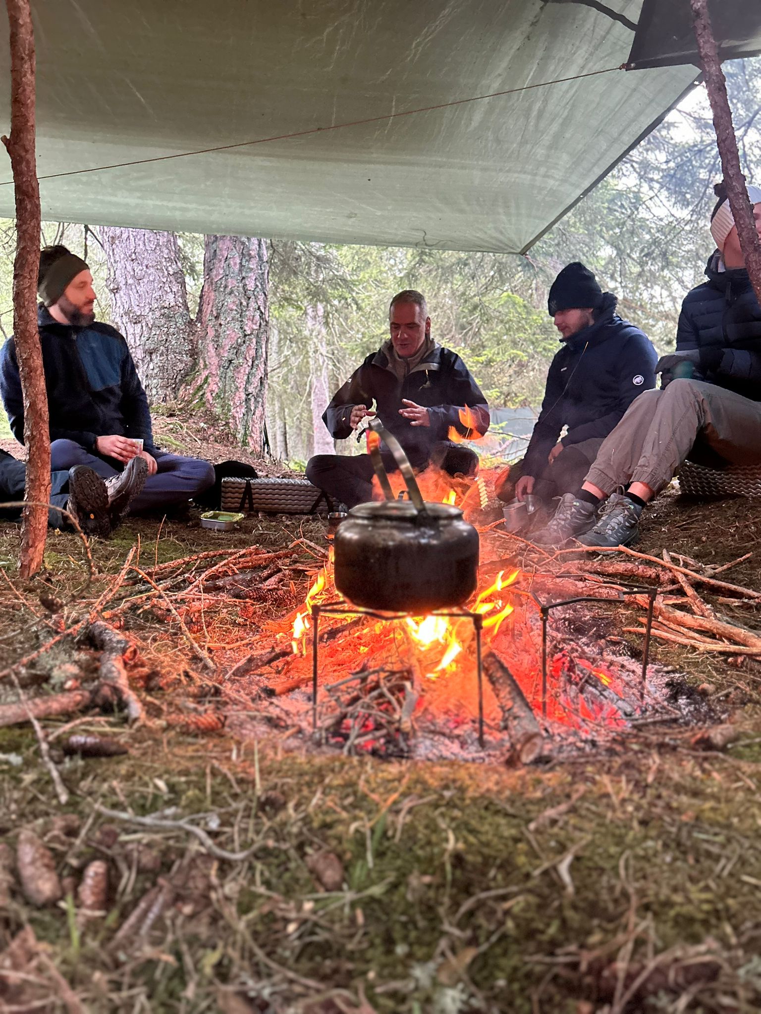 Männer im Gespräch am Lagerfeuer unter einem Tarp im Wald beim Ikigai Camp