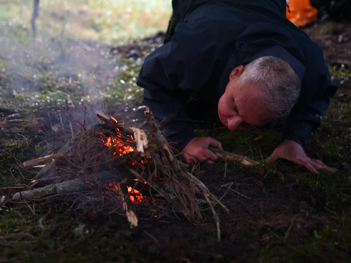 Mann entfacht Feuer am Waldboden beim Ikigai Camp