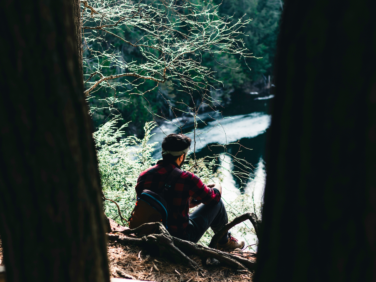 Unternehmer sitzt allein im Wald und blickt aufs Wasser – Symbol für innere Ruhe und Reflexion